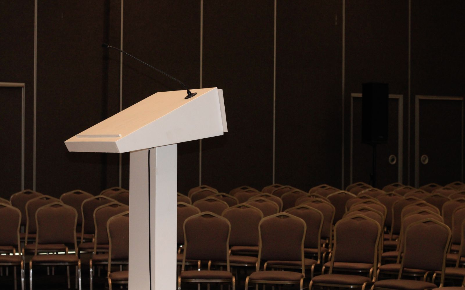 Conference lectern with a gooseneck microphone facing rows of chairs in an event room