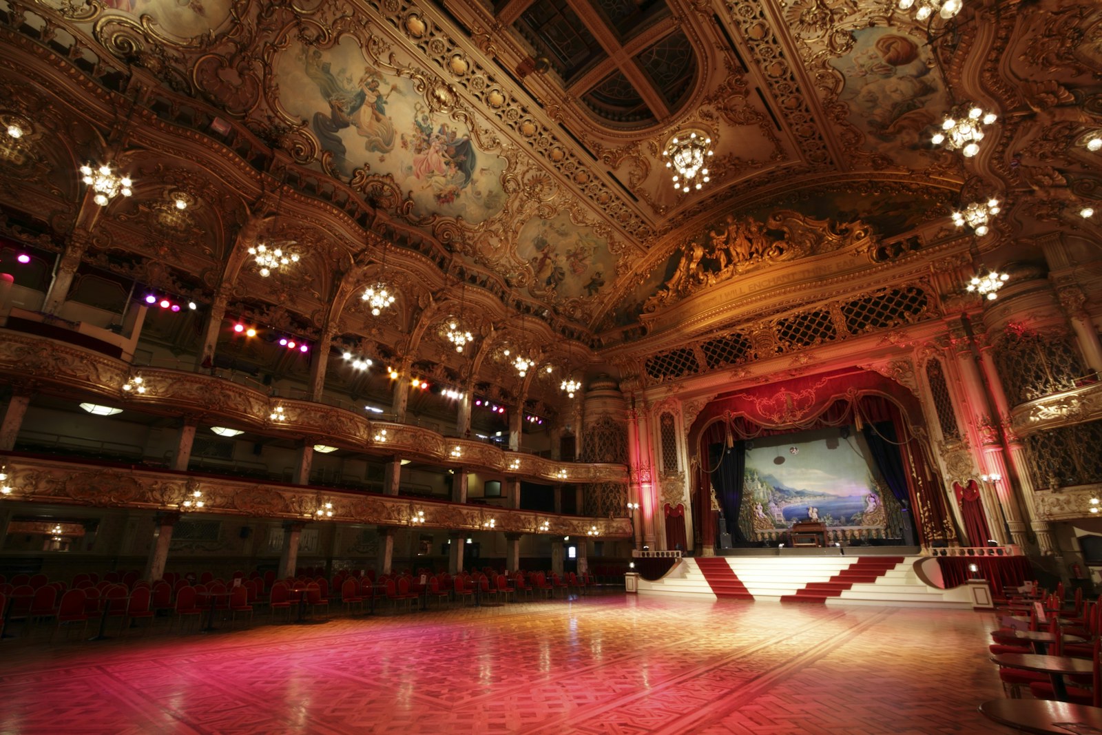 Large ornate ballroom with a performance stage, audience seating and architectural lighting